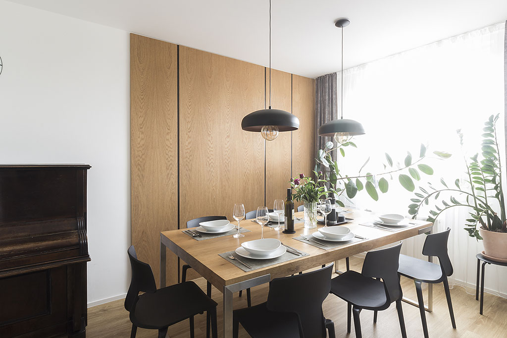 Design jídelního prostoru se stolem s masivní dubovou deskou a černými plastovými židlemi.