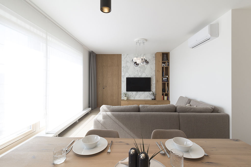 Návrh interiéru obývacího pokoje v bílo dubovém provedení s televizní stěnou a skrytými dveřmi.
