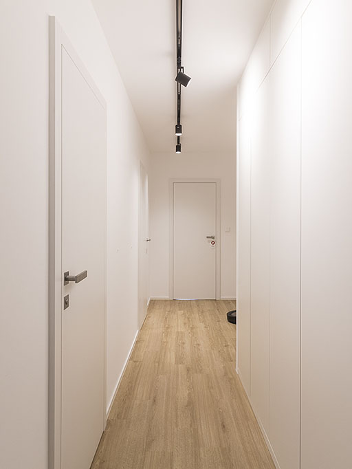 Realizace chodby s bezfalcovými dveřmi v bílé barvě a vestavnou bílou skříní doplněná vinylovou podlahou v dubovém desénu.