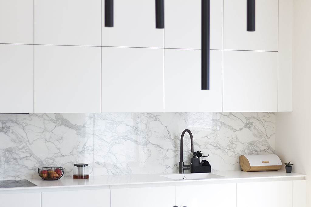 Návrhy kuchyní. Design interiéru bílé kuchyně s pracovní deskou z Corianu a integrovaným dřezem s černou baterií.