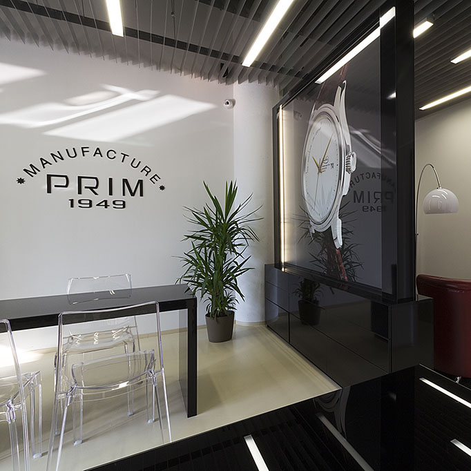 Design prodejny hodinek Prim s nábytkovými solitéry s osvětlenými propagačními materiály. Design prodejny je v černém provedení ve vysokém lesku.