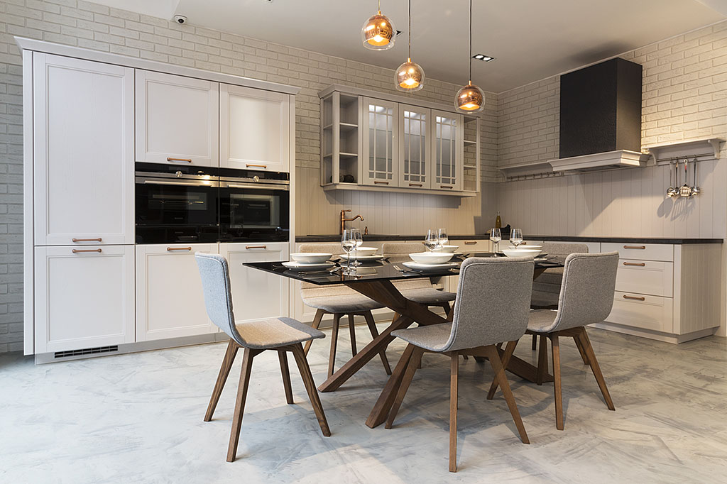 Design kuchyně v klasickém stylu doplněný o moderní prvky a jídelní stůl s židlemi s dubovými podnožemi a šedým polstrováním.