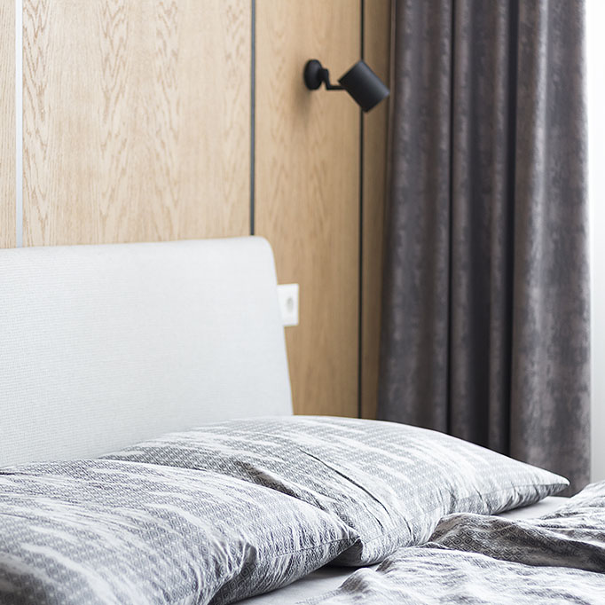 Návrh interiéru ložnice s šedou postelí doplněný šedými zatemňovacími závěsy.