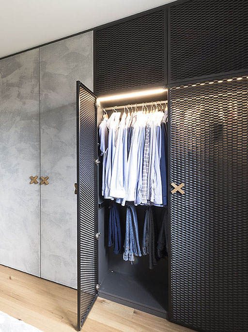 Design vestavné skříně v kombinaci betonové stěrky a perforovaných dveří v černé barvě.