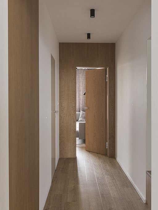 Návrh interiéru chodby s dubovou stěnou a dveřmi se skrytou zárubní, kterou jsou součástí stěny doplňuje vestavná skříň s dubovými dveřmi.