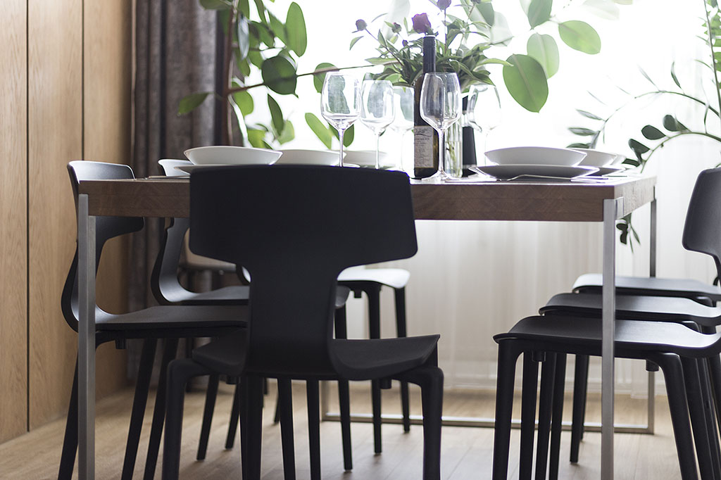 Jídelní stůl s deskou z masivního dubu a ocelovou podnoží doplněný o černé plastové jídelní židle italského výrobce.