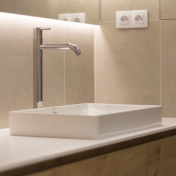 Design koupelny v béžovém stylu s umyvadlem na desce a vysokou stojánkovou baterií.