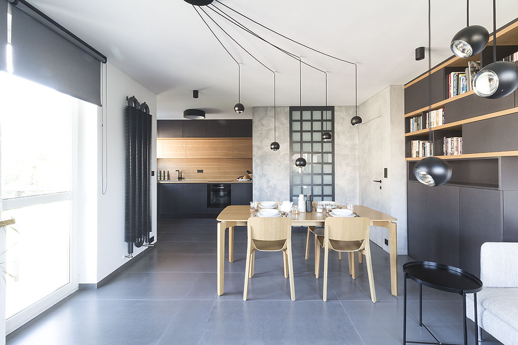 Návrh interiéru obývacího pokoje s kuchyní v industriálním designu s dubovým jídelním stolem, radiátorem Spiral v kombinaci s povrchy upravenými betonovou stěrkou doplňuje dlažba se škrábaným povrchem a nábytek na míru v provedení dubové dýhy a černě probarvené MDF desky Valchromat.