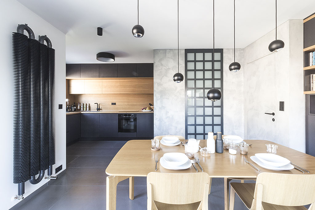 Design interiéru kuchyně s dubovým jídelním stolem a industriálním radiátorem. Návrh kuchyně je v provedení v kombinaci dubové dýhy a černě probarvené MDF desky.