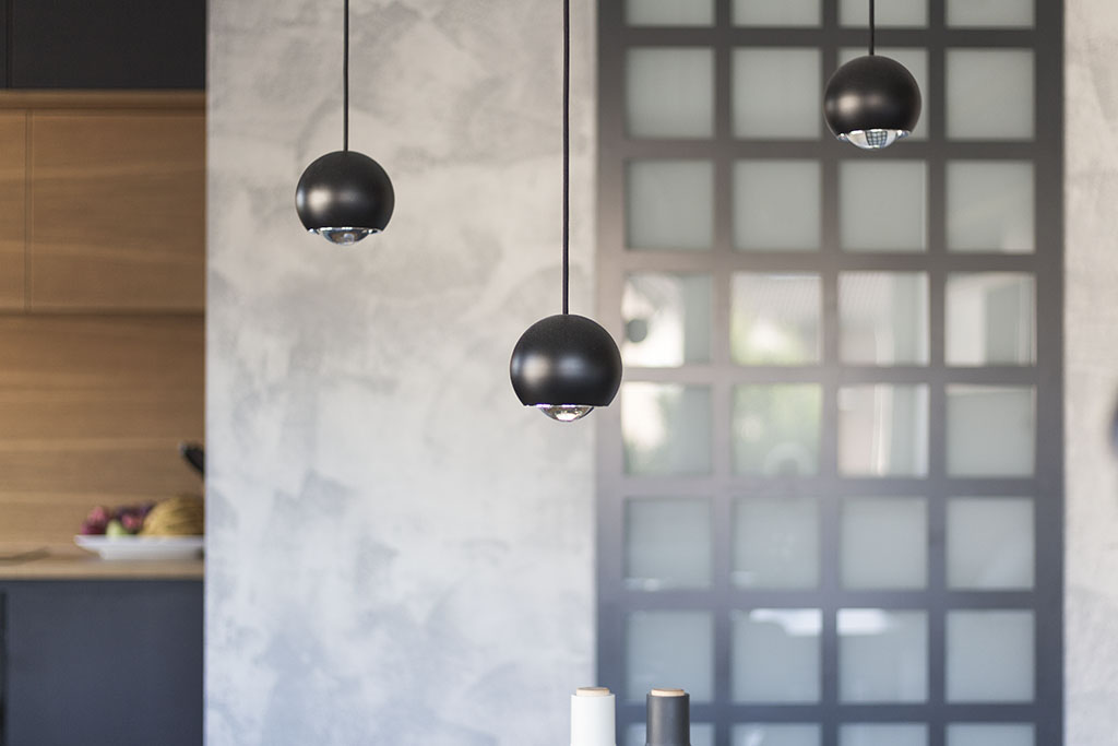 Návrh mezonetového bytu. Design interiéru osazený svítidly Lodes Spider v černém provedení v návaznosti na stěnu s betonovou stěrkou v šedé barvě a kovovým rámem s průsvitným sklem oddělujícím jídelní prostor od koupelny.