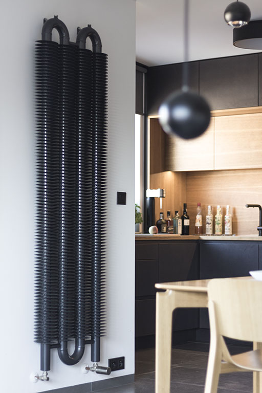 Návrh interiéru kuchyně s designovým radiátorem Isan Spiral. Design interiéru kuchyně je proveden v industriálním designu a kombinuje černou barvu a masivní dub.