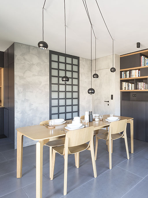 Design interiéru jídelny s dubovým stolem a židlemi od firmy Ton doplňuje stěna s šedou betonovou stěrkou a skleněnou stěnou s průhledem do koupelny. Součástí stěny se stěrkou jsou dveře se skrytou zárubní.